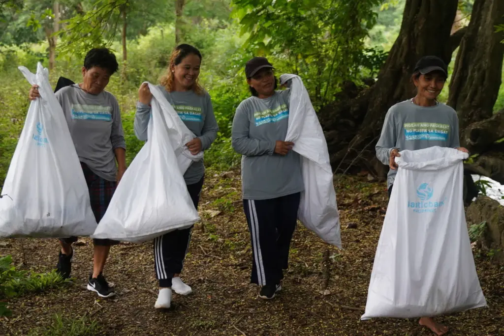 Plastic Bank collectors in the Philippines walk through a green forested area in their community, carrying bags of collected plastic 