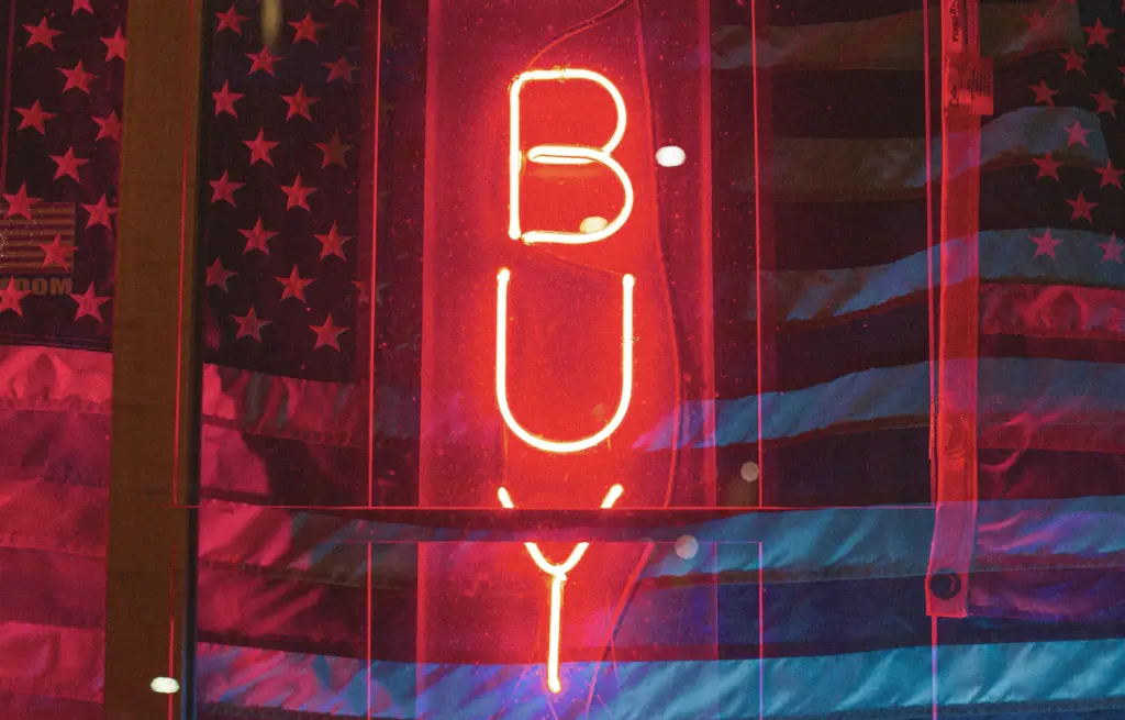 Double exposure of a neon sign that says Buy and an American flag