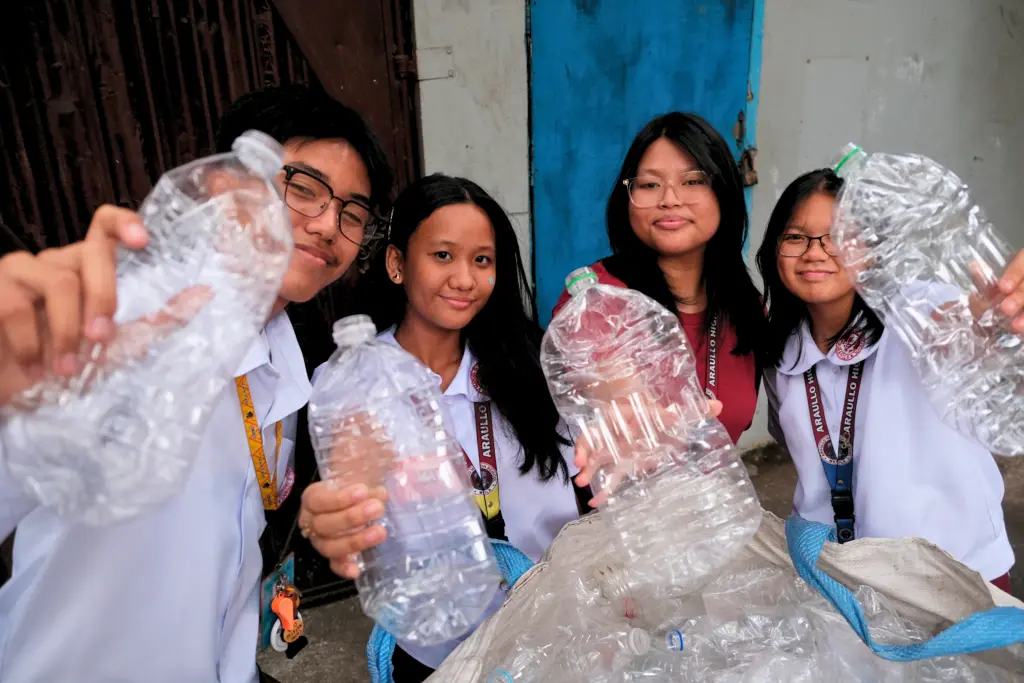 Four students holding up empty water bottles for recycling