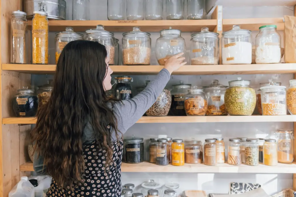 A woman reaching for supplies in a glass container on a kitchen shelf