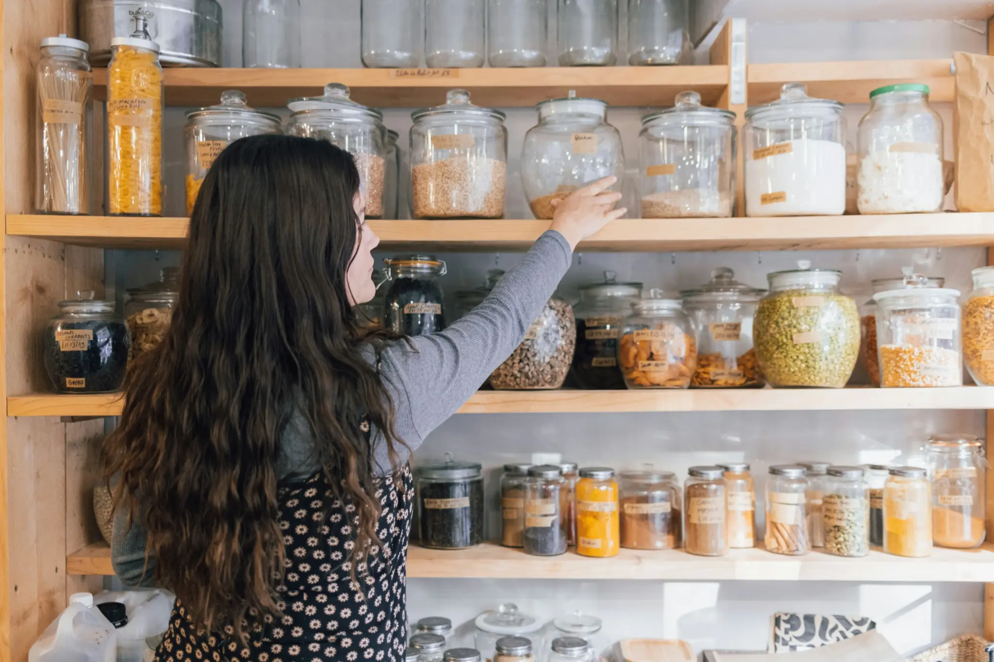 A woman reaching for supplies in a glass container on a kitchen shelf