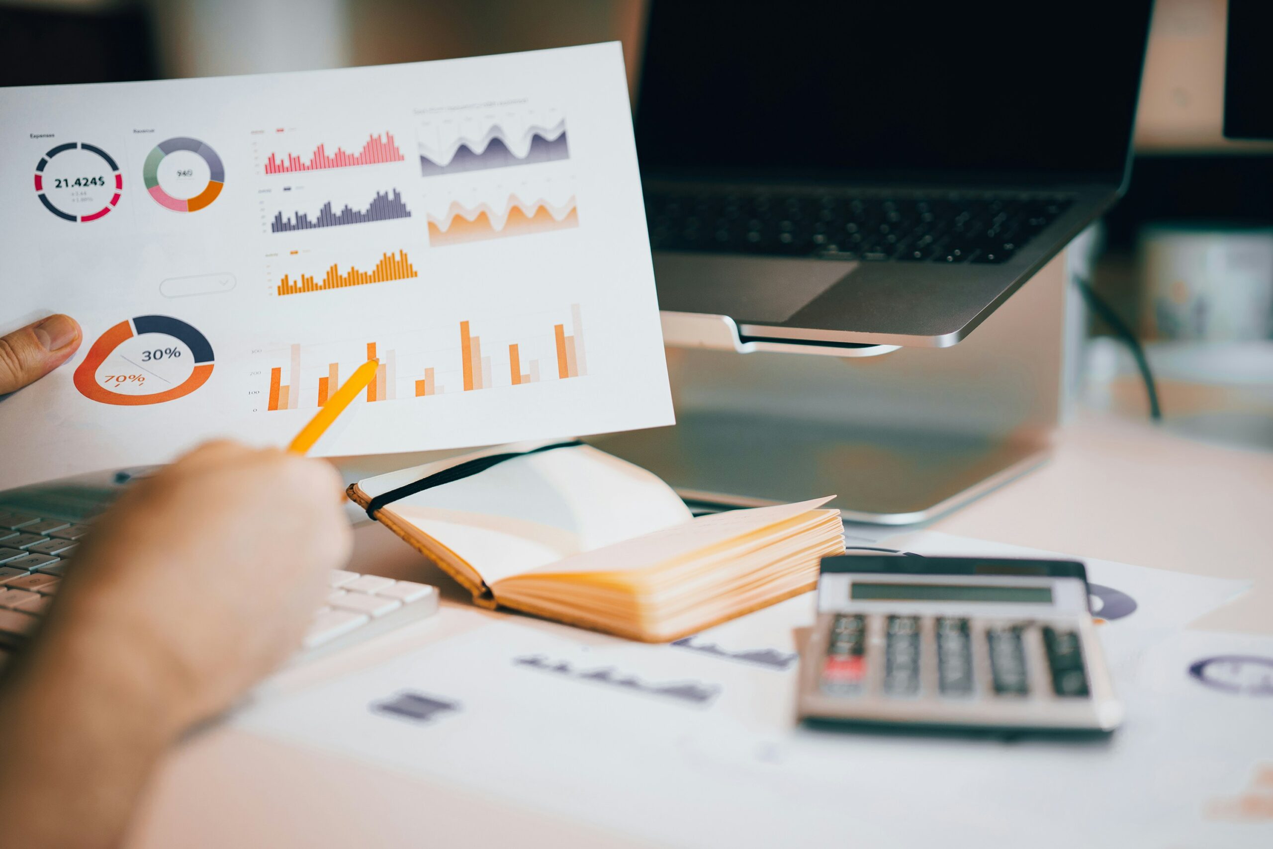 Statistics background with a person holding a paper with statistics and a laptop and a calculator.