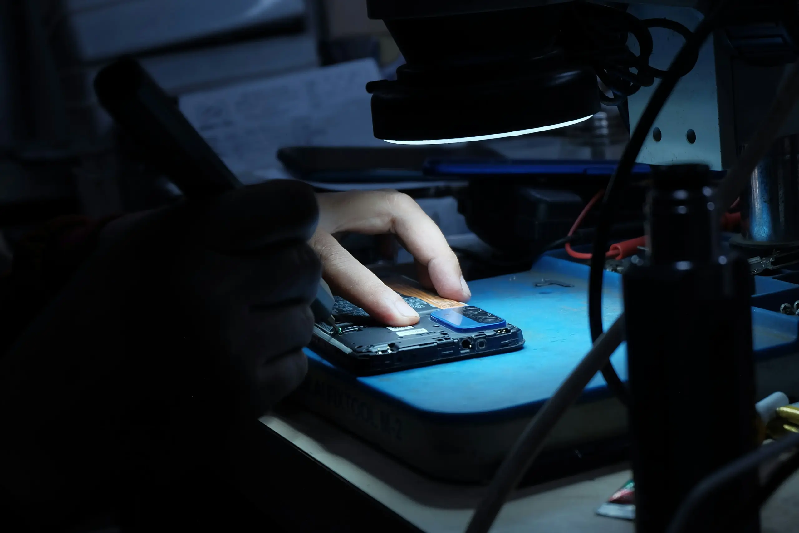 a technician checking a phone for repair under a magnifying light