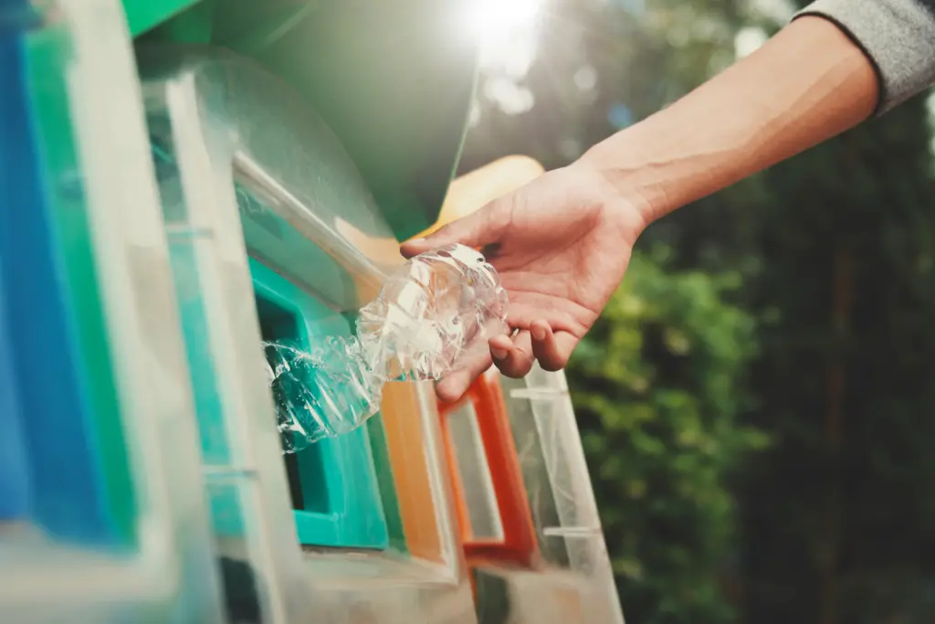 A plastic bottle being dropped into a recycling bin