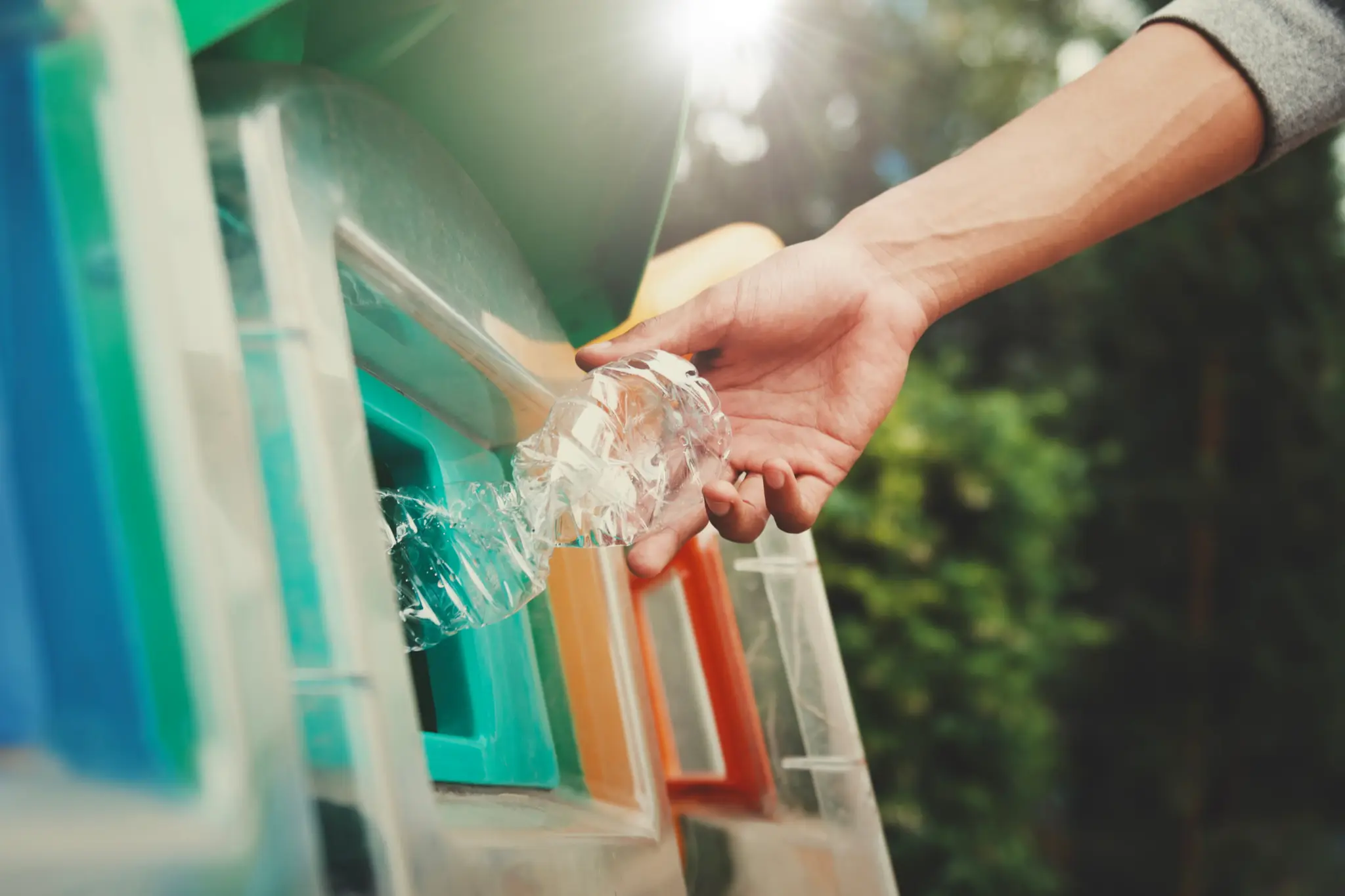 A plastic bottle being dropped into a recycling bin